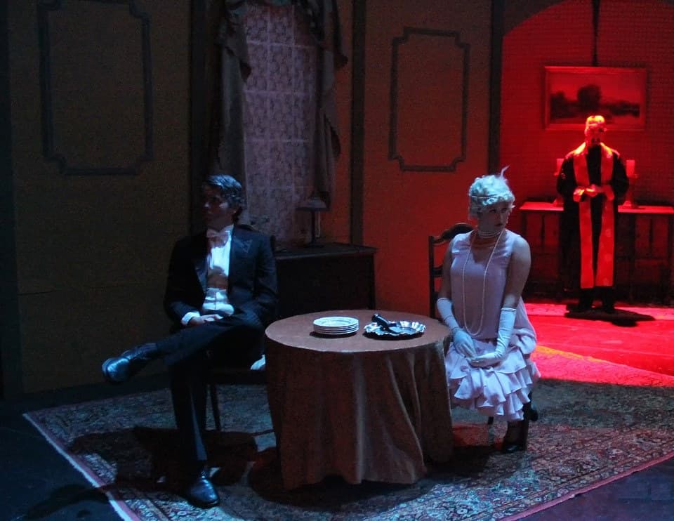 A red-lit drawing room, a flapper at the round table and a robed figure in the doorway — Bloody Murder, fall 2013.