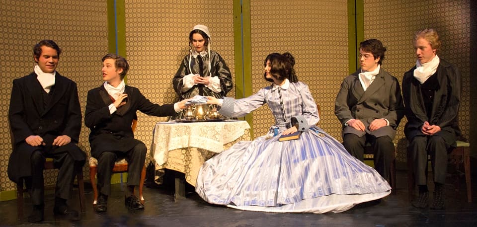 A 19th-century parlor: a woman in a striped blue hoop skirt holds court over the table while the men of letters look on — Charm, the 2014 festival one-act.